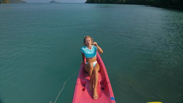 Pretty slim woman in elegant swimsuit lies in pink plastic kayak drifting on azure ocean at exotic resort upper view. Traveling to tropical countries. Girl is sailing on kayak in ocean, view above.