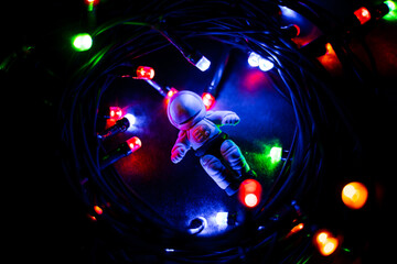 Astronaut's toy in a spacesuit lies among a bright garland. Space flights, toys for children made...