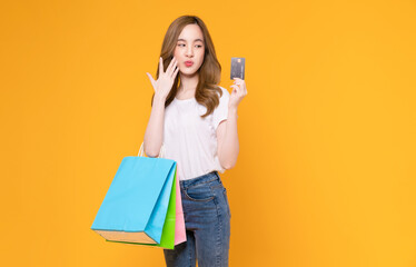 Beautiful Asian woman holding brown blank paper shopping bags and showing credit card on yellow background.