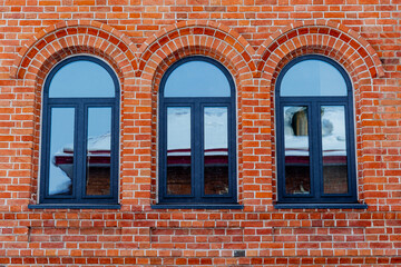 Fototapeta na wymiar Minimalistic shot of a brick wall with windows. Three arched windows with plastic frame. Red brick masonry. Building a house or wall. Repeating pattern
