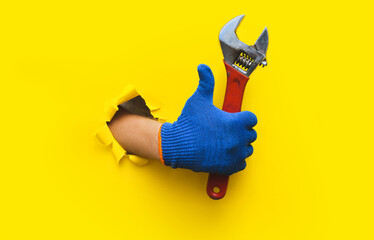 The right hand in a blue knitted glove holds a red wrench and gives a thumbs up (like). Torn hole...