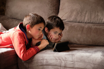 Two kids watching videos on the phone stretched out on the couch. Concept of screen addiction.1