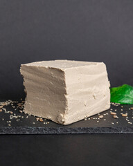 A large piece of sesame halva lies on a black serving board, a piece is cut off from the whole. National sweets, organic desserts concept 