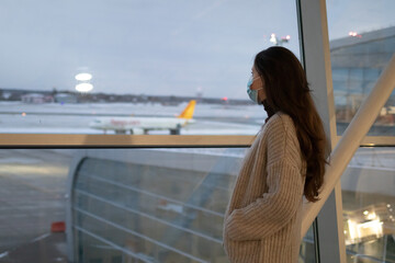Obraz premium A Caucasian woman is standing near the window in airport and looking at plane