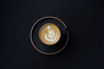 Cappuccino in a black mug on a black background Morning delicious takeaway coffee. Top view of the...