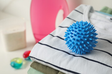 Blue dryer ball on stacked clean clothes, closeup. Space for text