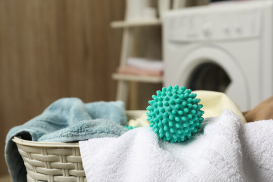 Turquoise dryer ball and towels in wicker basket near washing machine, closeup. Space for text
