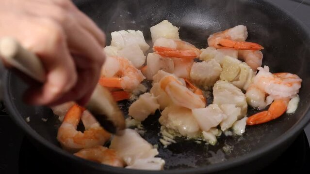 A cook fries white codfish and shrimp in a frying pan