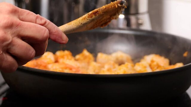 A cook fries white codfish and shrimp in a frying pan