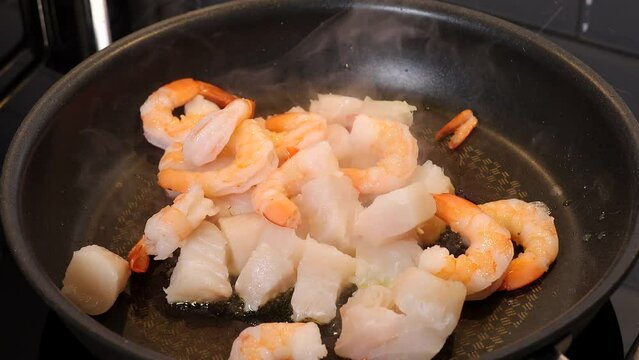 A cook fries white codfish and shrimp in a frying pan