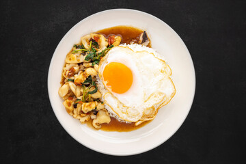 Khao Pad Ka Prao Pla Muek Kai Dao, Thai food, streamed rice topped with basil stir fried squid, octopus and fried egg in ceramic plate on dark tone texture background, top view, flat lay