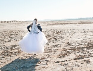 Fototapeta na wymiar Blonde girl in a wedding dress and a leather jacket in a rock style on a wild sandy beach