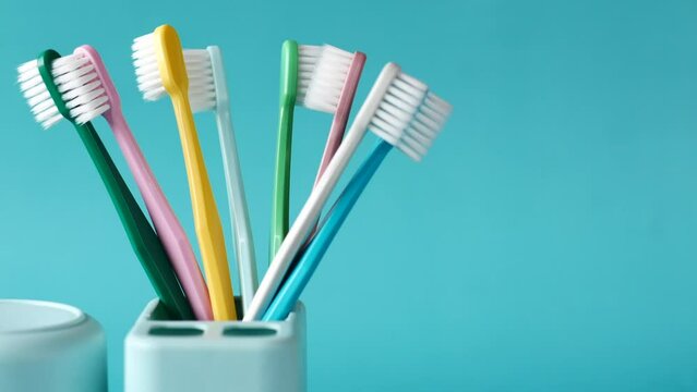  colorful toothbrushes in white mug against light green background 