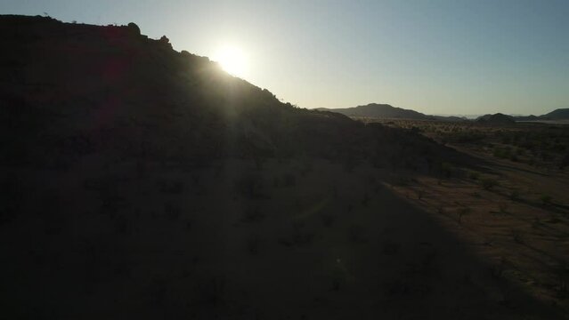 Hilly desert terrain, sun sitting low in afternoon; aerial trucking right