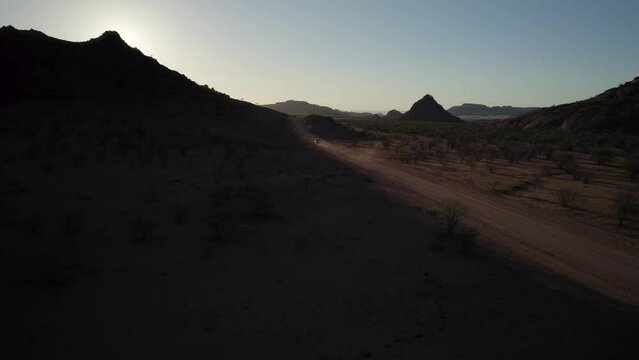Truck leaves dust cloud on dirt road through arid wilderness; sunset aerial