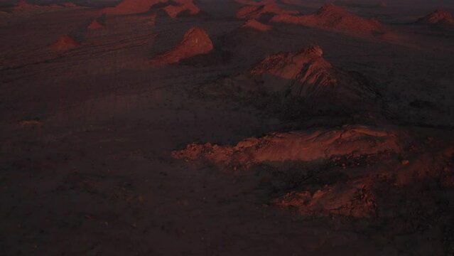 Red glow of rocky outcrops in desert wilderness at sunset; aerial reveal
