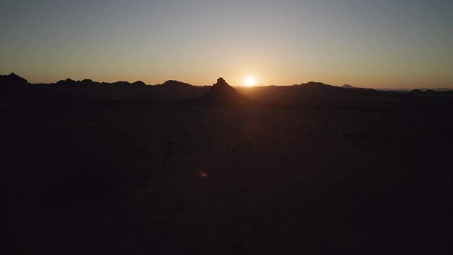 Golden sun orb just above horizon, sunset over desert landscape; drone