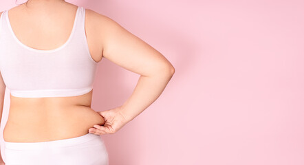 a fat girl holding a hand with excess fat on her stomach on a pink background. the concept of a woman's lifestyle with a diet to reduce the belly. recovery after childbirth. place for text