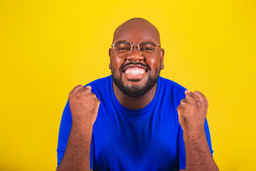 handsome afro brazilian man wearing glasses, blue shirt on yellow background. Closeup, closed...