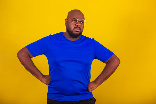 handsome afro brazilian man wearing glasses, blue shirt on yellow background. Nervous, angry, angry, angry, frustrated.