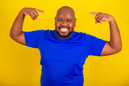 Handsome Afro Brazilian Man Wearing Glasses, Blue Shirt Over Yellow Background. Baldness Concept, Showing Head, Baldness, No Hair.