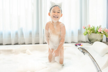 smiling happy asian child boy is playing with white foam in tub bath at home.