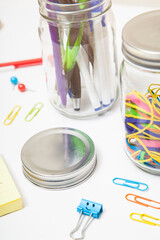 Clear Glass mason jars storing colorful office supplies on white desk