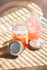 Glass mason jars with pink and red lemonade juice liquid drinks in sunlight