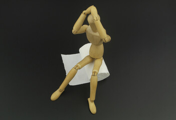 Wooden man mannequin figure sitting on roll of toilet paper on black background. Concept of problem with diarrhea, abdominal pain, food poisoning, intestinal infection.