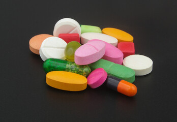 Many colorful pills and drugs on black table.