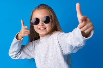 Little fashion girl in sunglasses against blue background