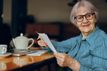 elderly woman with glasses sits at a table in front of a laptop Freelancer works unaltered