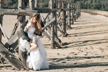 Blonde girl in a wedding dress and a leather jacket in a rock style on a wild sandy beach
