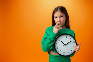 Beautiful teen girl holding big clock over orange background