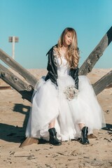Blonde girl in a wedding dress and a leather jacket in a rock style on a wild sandy beach