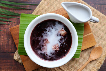 Black sticky rice pudding with taro and coconut milk at top view of wood table, Black glutinous rice - Thai dessert called Khao Nieow Dam 