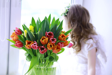 Beautiful girl in white dresses with a magnificent bouquet of the first tulips. International Women's Day. Girl with tulips.