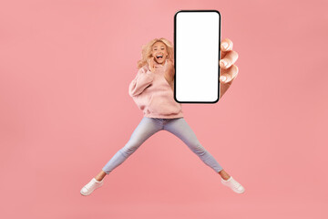 Full length of excited woman jumping and showing smartphone with empty space for mobile app or...