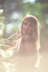 Blonde girl in a light airy dress, barefoot at dawn in a summer forest
