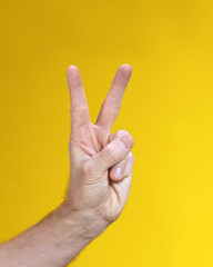 Naklejka premium Male two fingers up on hand gesture isolated on yellow background. Victory sign, V sumbol.
