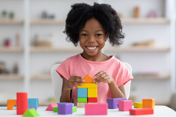 Happy little black girl playing with colorful wooden blocks