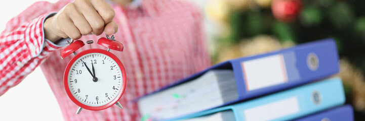 Woman holding many folders with documents and red alarm clock near new year tree closeup