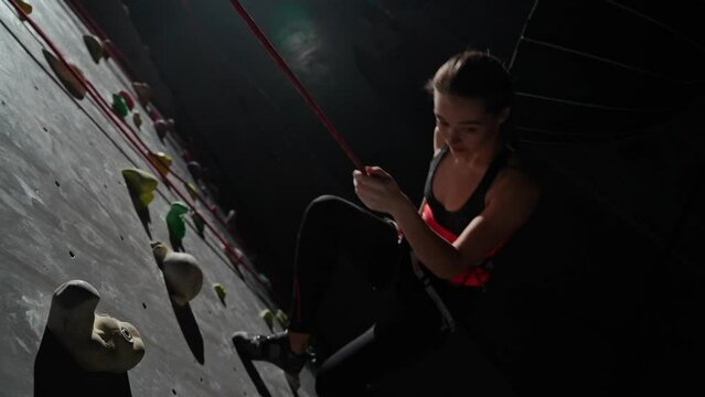 Female professional climber training on a climbing wall, practicing rock-climbing and descends from the cliff using insurance.