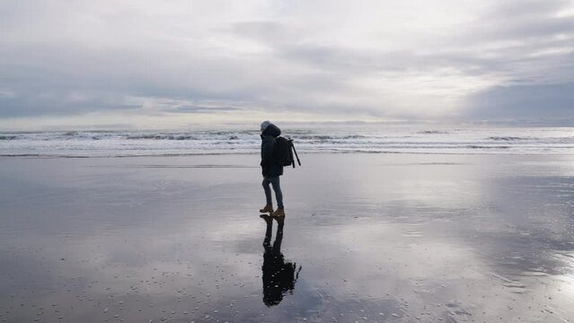 Man With Backpack Walking Along Wet Beach Towards Vestrahorn