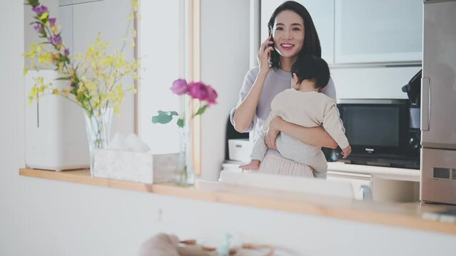 眠る赤ちゃんを抱っこしながらスマートフォンで電話をするお母さん