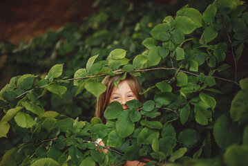 the girl cheerfully looks out of the bushes, only the eyes are visible, close-up