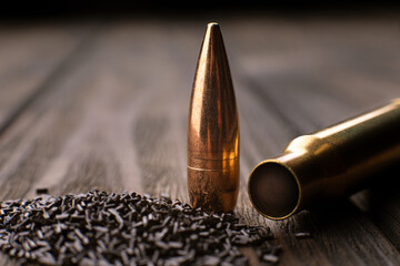 Macro shot of a cartridge, cartridge case and gunpowder on a wooden background with limited depth of field, soft focus - obrazy, fototapety, plakaty