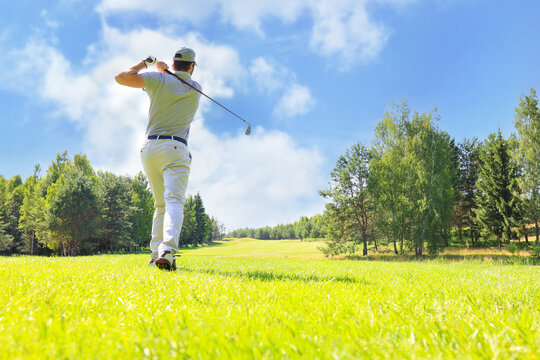 Full length of golf player playing golf on sunny day. Professional male golfer taking shot on golf course.