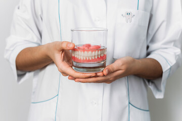 Prosthesis in a glass with a solution. Dental prosthesis care. Full removable plastic denture of the jaws. Two acrylic dentures. Upper and lower jaws with fake teeth. Dentures or false teeth, close-up