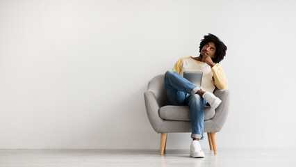 Interesting Offer. Thoughtful Young Black Man With Digital Tablet Resting In Chair